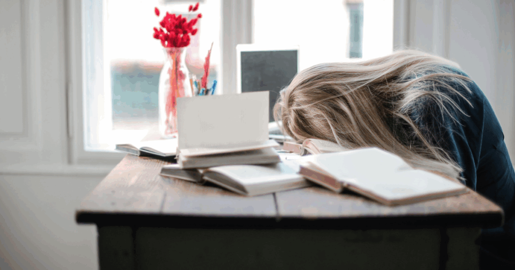 Supporting someone with depression: Exhausted woman with head on books, illustrating the challenges of depression support.