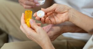 - Los Angeles Mental Health Close-up of hands holding an orange prescription bottle and its cap, with yellow pills inside and one tablet on the cap about to be taken.