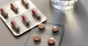 - Los Angeles Mental Health Blister packs with pink-and-beige capsules and round brown tablets on a gray surface near a glass of water.